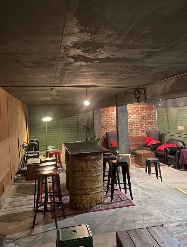Industrial style function room at Neighborhood Pizza and Pasta with communal seating, a repurposed barrel table, and warm hanging lights.